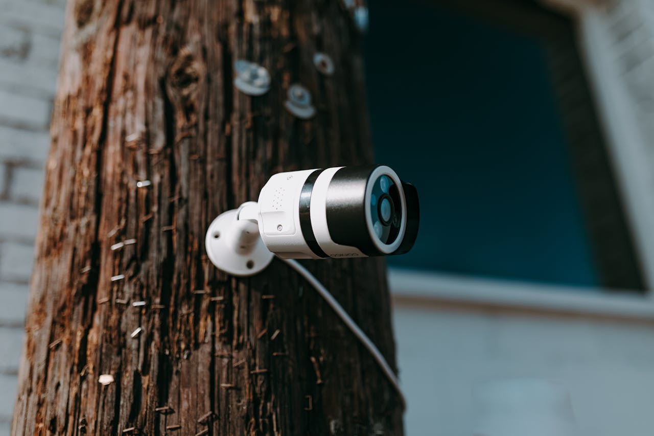 Home 1 Close-up of a modern security camera mounted on a wooden post outdoors.
