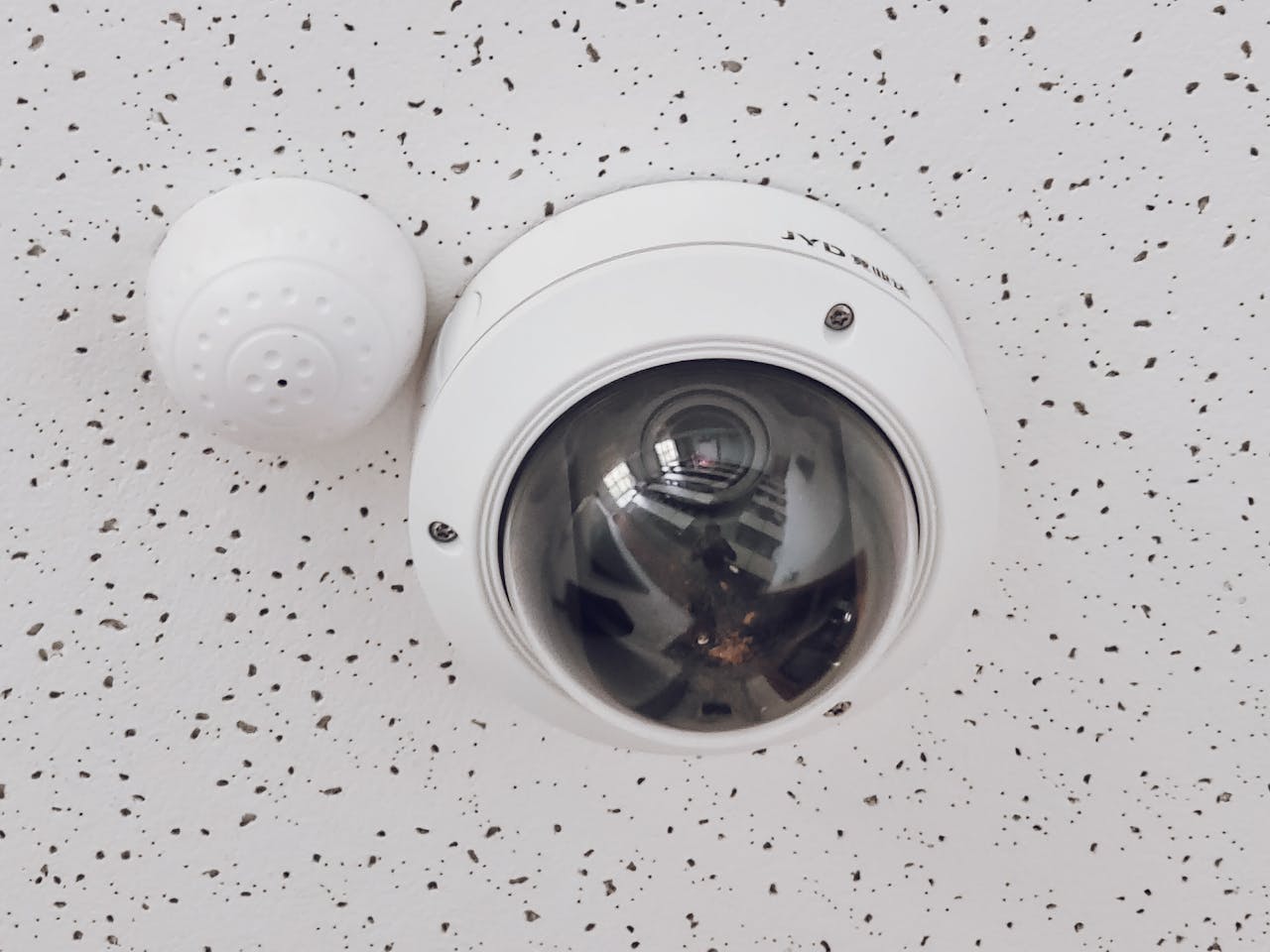 Home 3 Close-up of a round dome surveillance camera installed on a speckled ceiling for security monitoring.